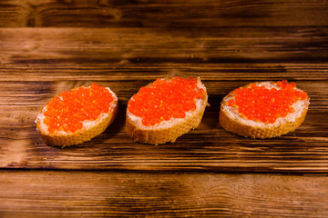 Sandwiches with red caviar on wooden table