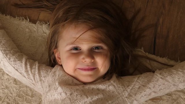 Cute little child girl play at home roll lie on a floor rug nice watch to camera