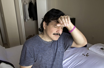 Man with hand to head while sitting on bed