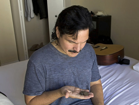 Man looks at his money change while sitting on his bed