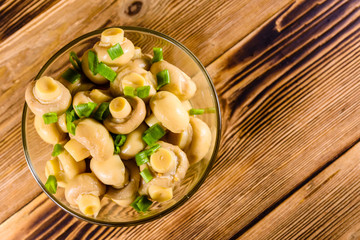 Canned mushrooms in a glass bowl on wooden table. Top view