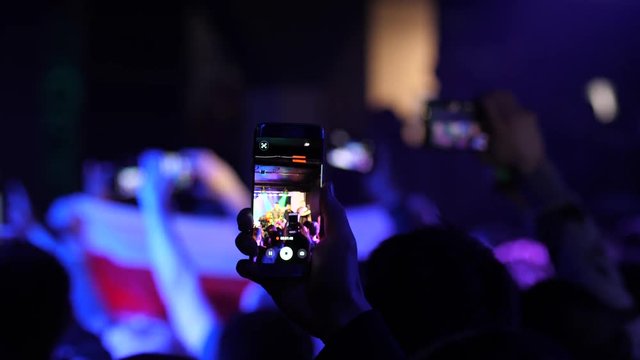 Smart phone in hand spectator in crowd shoot video of concert performance