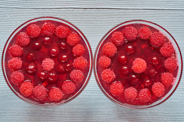 Cold raspberry jelly with fresh cherries in two glasses. Freshness healthy summer dessert on the gray concrete background. Top view