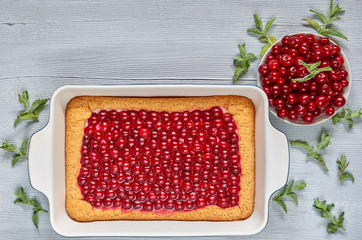 Delicious cherry pie in the baking dish on the gray kitchen table with copy space. Homemade summer tart decorated with raw ingredients - cherries and mint leaves. Top view