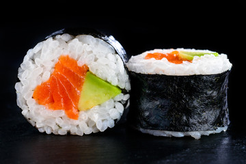 Tasty sushi rolls in nori with avocado and red fish on dark back