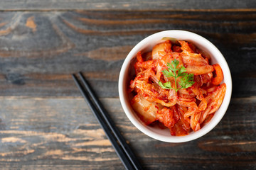 Kimchi cabbage in a bowl with chopsticks for eating on wooden background, top view, Korean food - obrazy, fototapety, plakaty