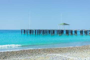 A lone pier with blue water and a gazebo with a colored roof