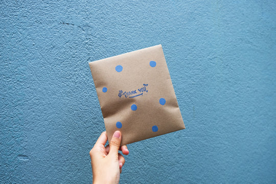 Female hand holding a envelope gift with text " THANK YOU" on blue background