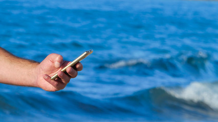 Male hand using smartphone on the beach