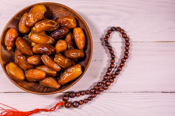 Date fruits and rosary on wooden table. Top view