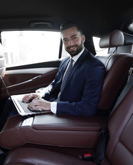 smiling businessman sitting in the back seat of a prestigious car