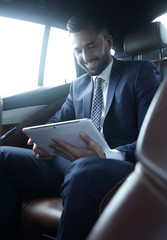 businessman with a digital tablet sitting in the back seat of a car