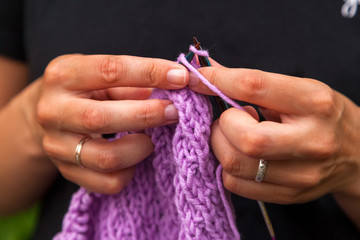 Close-up Young woman  in black t-shirt knits with knitting needles lilic sweater from natural woolen threads