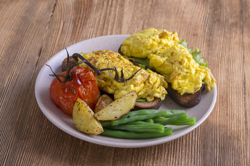 Egg omelette on a piece of black bread with red tomatoes, green beans and fried potato on a wooden table, close up. Breakfast concept