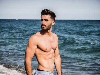 Handsome young man standing at a beach, relaxed, shirtless wearing boxer shorts