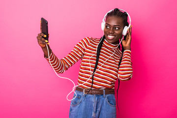 Beautiful afro american woman with listining to music and dancing on pink background