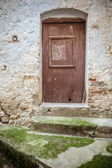 Old wooden door, moss-covered steps and stone eroded wall. Front door