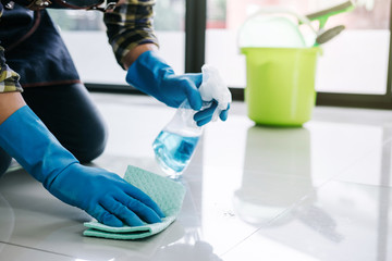 Husband housekeeping and cleaning concept, Happy young man in blue rubber gloves wiping dust using a spray and a duster while cleaning on floor at home