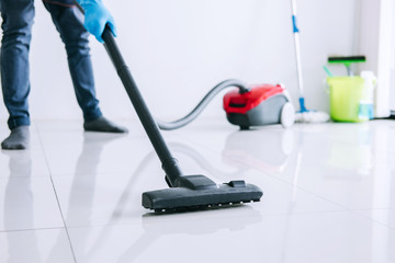 Housekeeping and housework cleaning concept, Happy young man in blue rubber gloves using a vacuum cleaner on floor at home