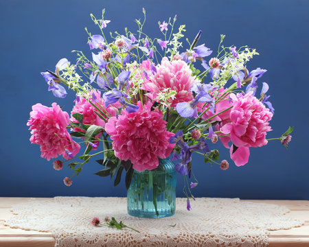 bouquet of pink peonies and other flowers in a glass vase on the table.