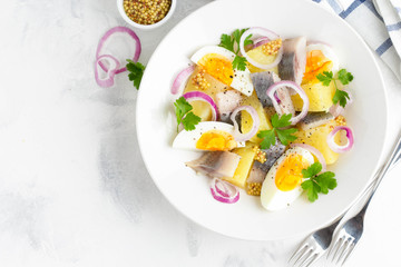 Potato salad with herring, egg, onion, tasty snack with mustard in white plate