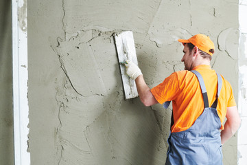 Renovation at home. Plasterer smoothing plaster on wall. - obrazy, fototapety, plakaty