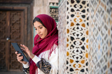 Muslim woman working on tablet in traditional clothing with red headscarf on her head