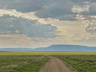 Fototapeta premium Vanishing dirt road in savanna against mountain and cloudy sky background. Serengeti National Park, Tanzania, Africa. 