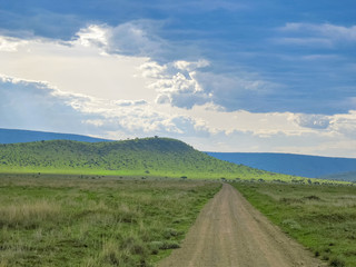 Vanishing dirt road in savanna against mountain and cloudy sky background. Serengeti National Park, Tanzania, Africa. 