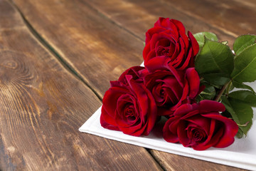 Five red roses on a white cloth on a wooden table. Romantic concept. Flat lay, top view.