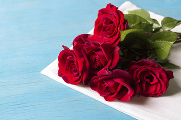 Bouquet of red roses on a white napkin and blue wooden background. Copy space. Romantic gift for Valentine's Day holiday