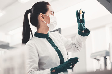 DNA. Profile of experienced concentrated doctor holding blood sample and scrutinizing it while...