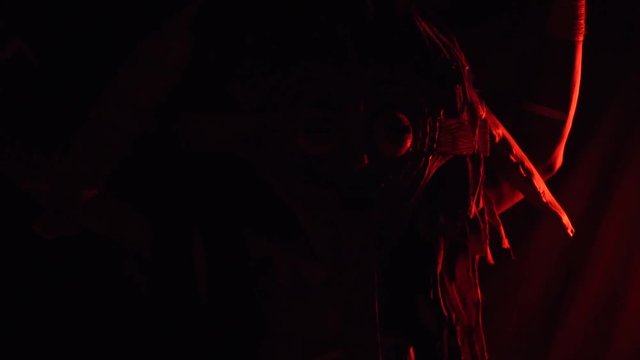 An African man in a wooden mask and mysterious patterns on his body dances in red light, slow motion