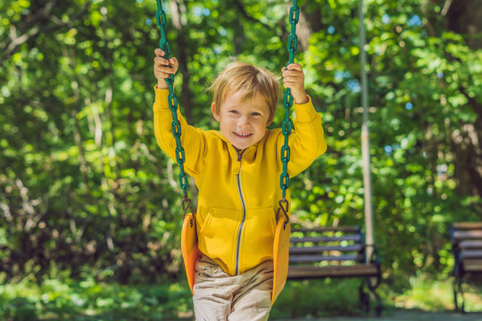 A boy in a yellow sweatshirt sits on a swing on a playground in autumn
