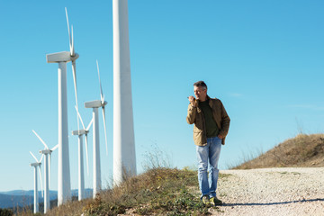 Man talking with portable radio transmitter outdoor over the wind turbines, image toned. Windmill...
