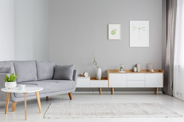 Real photo of a spacious living room interior with gray sofa standing between a wooden table and...