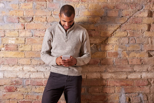A happy handsome young man using his smartphone in a sweater.