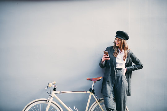 Woman Standing Against The Wall And Using Smart Phone For Texting. Next To Her Yellow Bicycle.