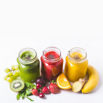 Three glass jars with various smoothies and ingredients on a whi