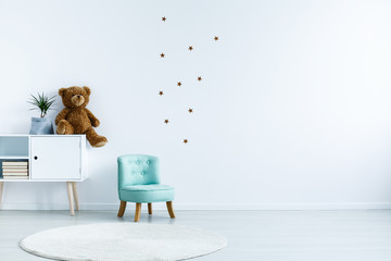 Small light blue armchair for kid standing in white room interior with stars on the wall, white rug...