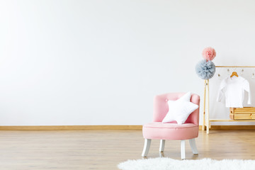 Pink chair with star shaped cushion standing in bright baby room interior with wooden hanger with...