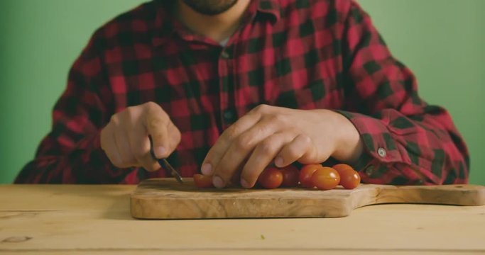 Young man cutting tomatoes against green screen