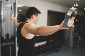 Young strong man doing exercises on the simulator at the gym. Toned image