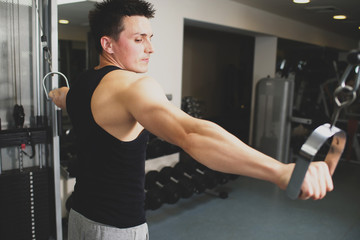Young strong man doing exercises on the simulator at the gym. Toned image