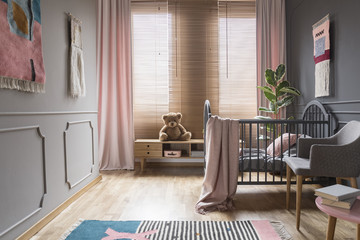 Drapes and blinds on windows in child's bedroom interior with pink blanket on bed. Real photo