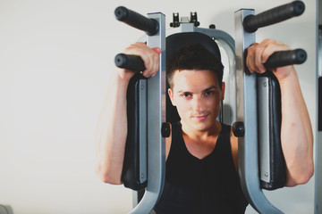 Young strong man doing exercises on the simulator at the gym. Toned image
