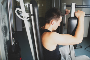 Young strong man doing exercises on the simulator at the gym. Toned image