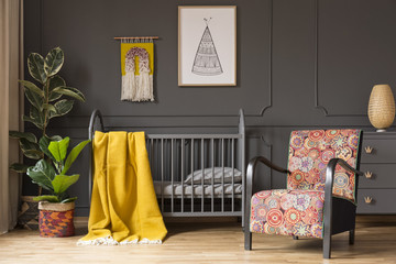 Patterned armchair next to kid's bed with yellow blanket in bedroom interior with plants. Real photo