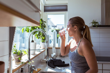 Woman drinking tap water in kitchen