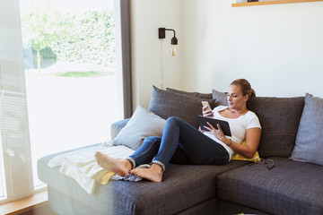 Full length of woman using digital tablet and mobile phone while leaning on sofa
